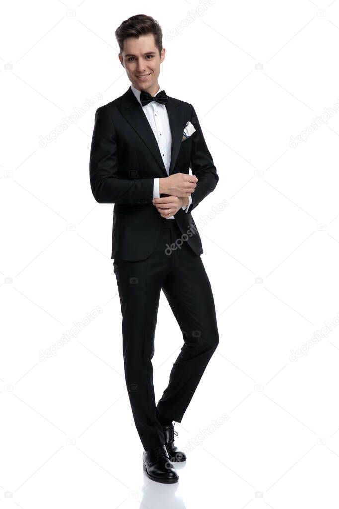 happy elegant groom in tuxedo fixing shirt and smiling