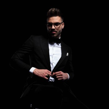 Gözlüklü işadamı oturuyor ve ceketini düzenliyor.