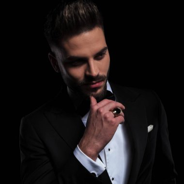 Siyah smokin giyen işadamı ayakta duruyor ve çene kalemlerine dokunuyor.