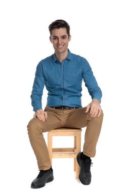 Gülümseyen ve avuçlarını dizlerinde tutan mutlu genç adam.