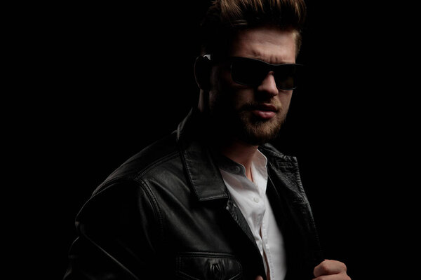 casual man wearing leather jacket standing and pulling his jacke