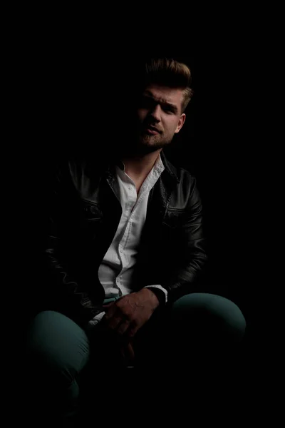 casual man wearing leather jacket sitting in the shadows