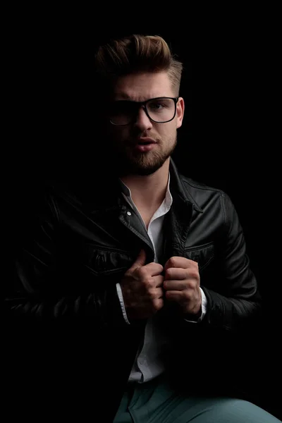 Casual man wearing eyeglasses sitting and pulling his jacket — Stock Photo, Image