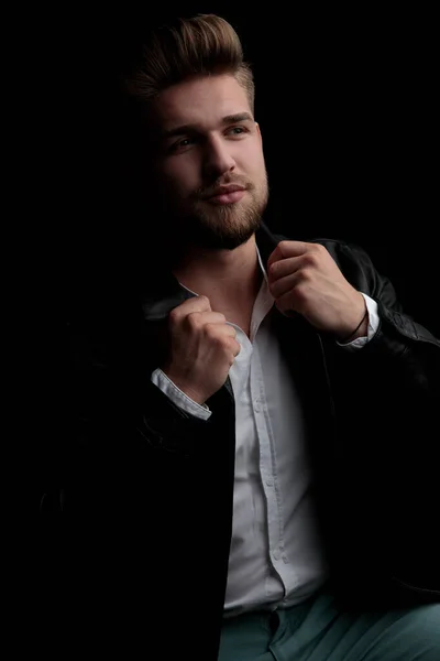 Casual man wearing leather jacket sitting and fixing his collar — Stock Photo, Image