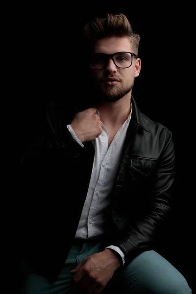 Casual man wearing leather jacket sitting and fixing collar — Stockfoto