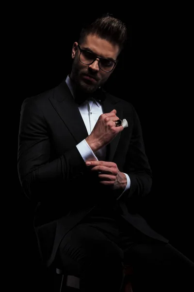 Businessman wearing eyeglasses sitting and fixing his sleeve — Stock Photo, Image