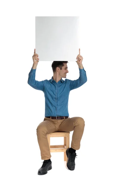 Happy young man holding empty board above head — Stockfoto