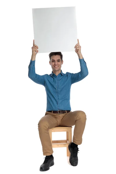 Happy young man holding empty board above head — Stockfoto