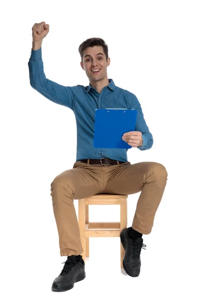 Happy young man holding clipboard and celebrating victory — Stockfoto