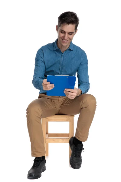 Hombre casual inteligente sonriendo y leyendo notas desde el portapapeles —  Fotos de Stock