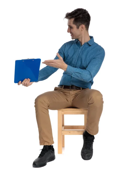 Joven feliz sosteniendo y presentando portapapeles a un lado — Foto de Stock