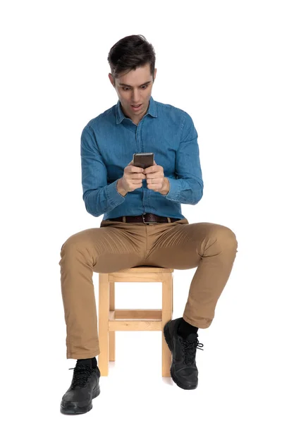 Shocked smart casual man holding phone and sitting — Stock Photo, Image