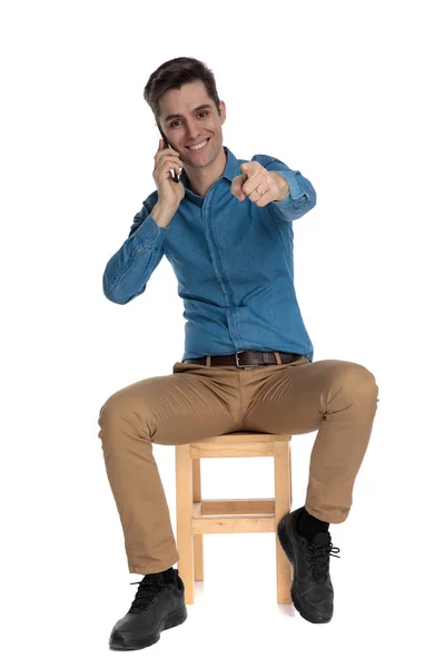 Happy young man talking on the phone and pointing finger — Stockfoto