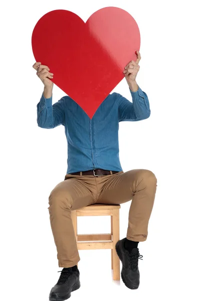 Mladý muž skrývající tvář za červeným srdcem — Stock fotografie