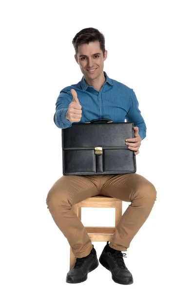 Happy young man making thumbs up sign and holding suitcase — Stockfoto