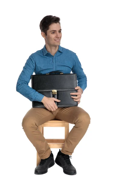 Smiling young man holding suitcase and looking to side — Stockfoto