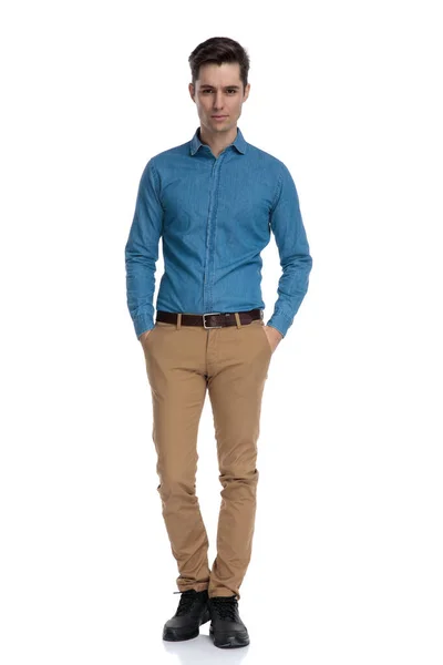 Счастливый молодой человек в голубой рубашке, держась за руки в карманах — стоковое фото