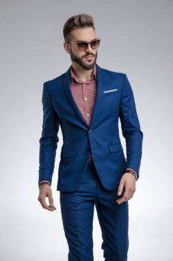 Mavi takım elbiseli, güneş gözlüğü takan ve poz veren havalı adam.