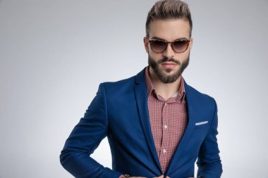 Mavi takım elbiseli seksi genç manken güneş gözlüğü takıyor ve poz veriyor.