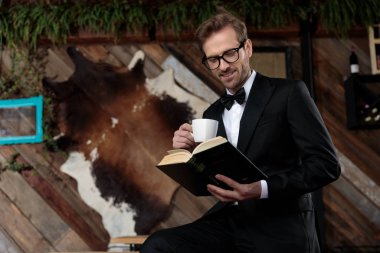 Elinde kahve fincanı tutan ve kitap okuyan bir damat.