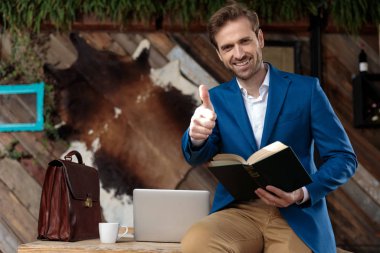 Neşeli iş adamı elinde bir kitap tutuyor ve başparmağını kaldırıyor.