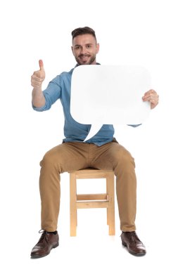 Konuşma baloncuğu tutan ve baş parmak işareti yapan mutlu genç adam.