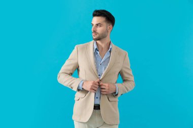 Seksi genç adam ceketini ayarlıyor ve yanına bakıyor.