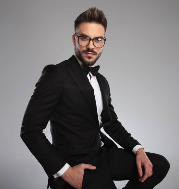 Kendine güvenen bir model, elini cebinde tutuyor, smokin giyiyor.