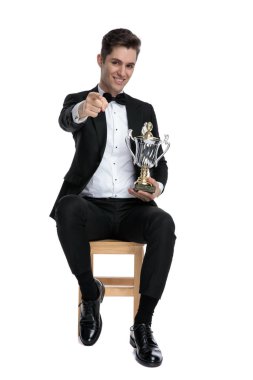 Mutlu genç model kupa tutuyor ve parmağıyla işaret ediyor.