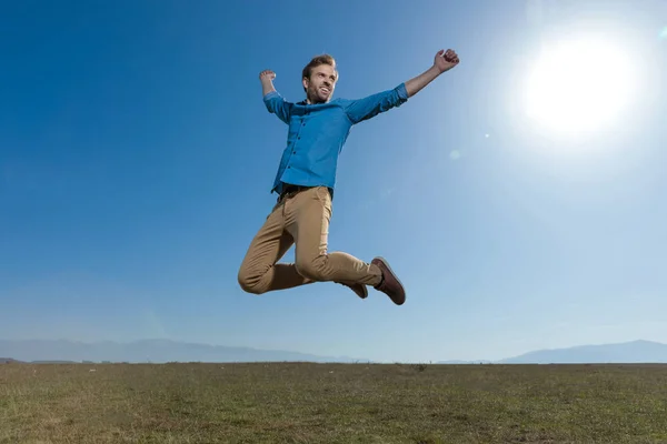 Casual man jumping with hands in the air carefree — Stock Photo, Image