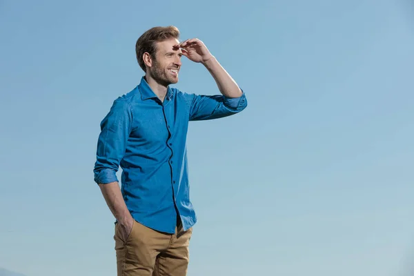 Casual man standing with hand in pocket and protecting eyes — Stock Photo, Image