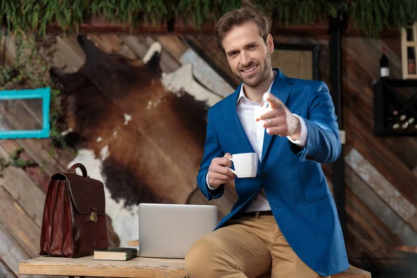 Neşeli iş adamı ileri doğru işaret ediyor ve elinde kahve fincanı tutuyor. — Stok fotoğraf