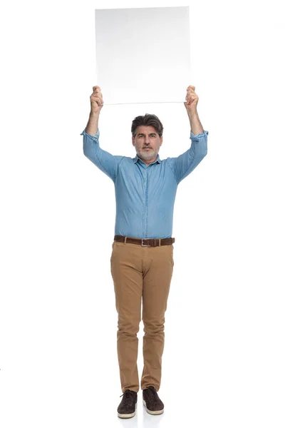 Zelfverzekerde toevallige man die een leeg reclamebord boven zijn hoofd houdt — Stockfoto