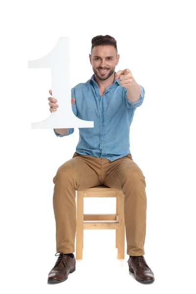 Joven feliz sosteniendo el signo número uno y señalando con el dedo —  Fotos de Stock