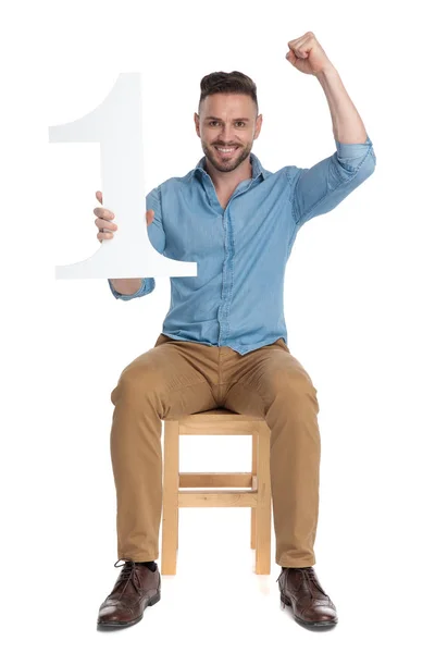 Взволнованный молодой человек держит знак номер один и празднует — стоковое фото
