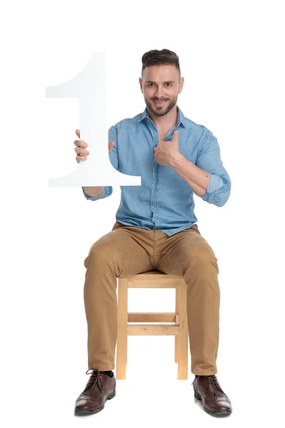 Счастливый молодой человек, держащий знак номер один и указывающий пальцем — стоковое фото