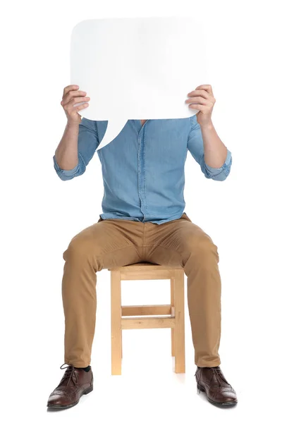Young casual man hiding behind speech bubble — Stock Photo, Image
