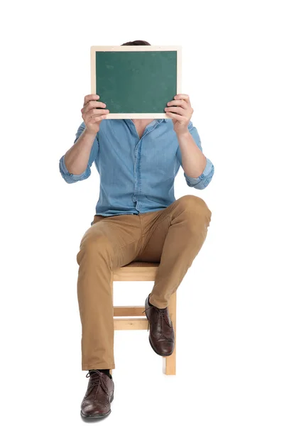 Young casual man hiding face behind green board — Stock Photo, Image