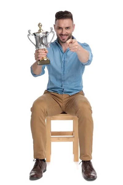 Young casual man pointing finger and holding trophy — Stock Photo, Image