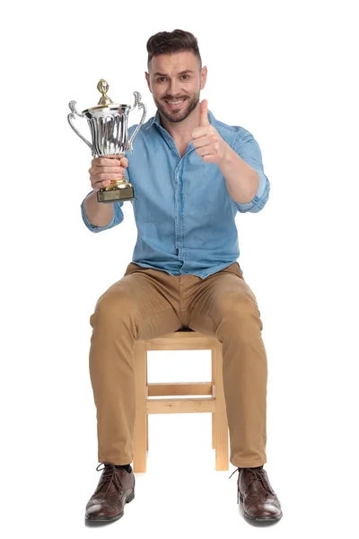 Gelukkig jong casual man holding trofee en het maken van duimen omhoog teken — Stockfoto