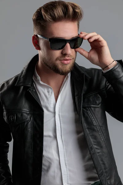 Sexy young man wearing leather jackt and fixing glasses — Stock Photo, Image