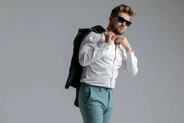 Sexy cool guy holding leather jacket and fixing shirt — Stock Photo, Image