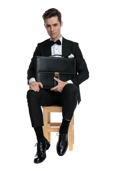 Ernster junger Mann sitzt und Koffer hält — Stockfoto