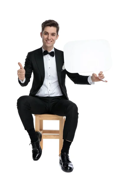 Smiling young man holding speech bubble and making thumbs up sig — Stock Photo, Image