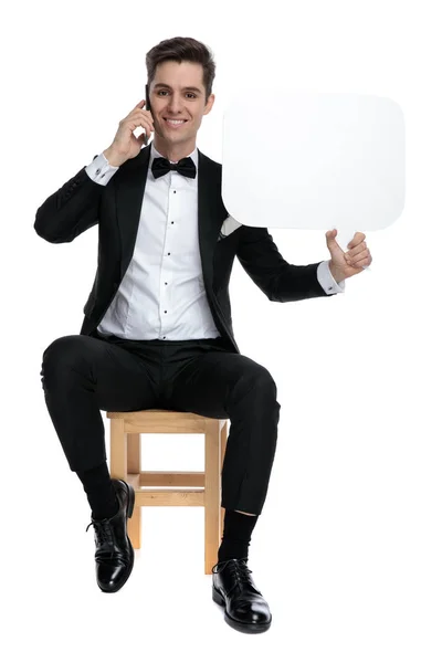 Happy young groom holding speech bubble and talking on the phone — Stock Photo, Image