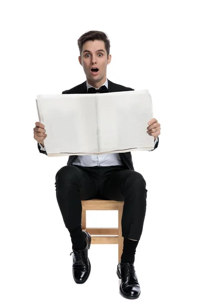 Sorprendido joven modelo leyendo periódico y sentado — Foto de Stock