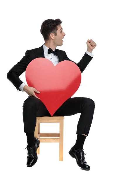 Joven elegante hombre sosteniendo gran corazón rojo y celebrando la victoria — Foto de Stock