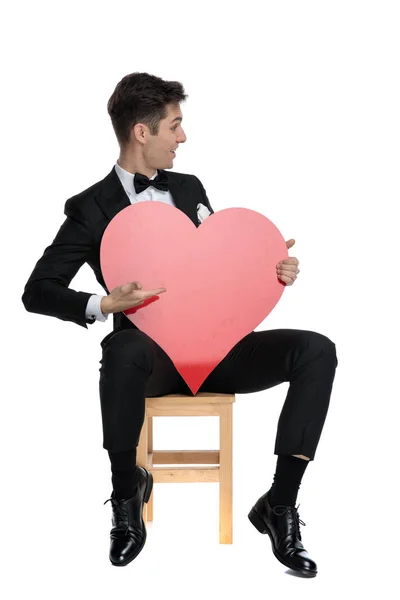 Feliz joven elegante hombre presentando a un lado grande corazón rojo — Foto de Stock