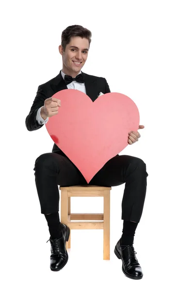 Happy young groom holding big red heart and smiling — Stock Photo, Image
