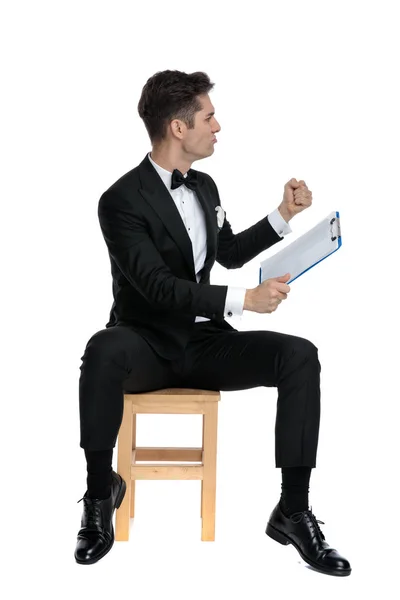 Joven elegante hombre sosteniendo portapapeles y celebrando la victoria —  Fotos de Stock